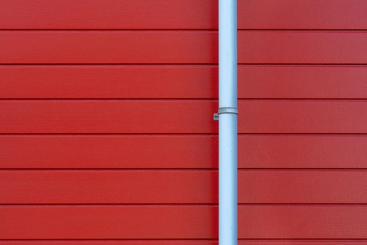 A white downpipe against a red exterior wall